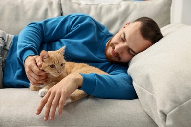 Photo of Man petting cute ginger cat on sofa at home