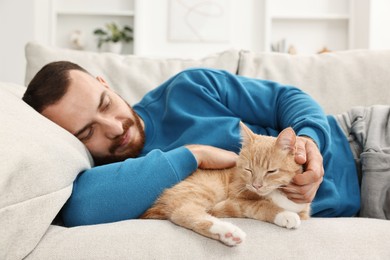 Man petting cute ginger cat on sofa at home