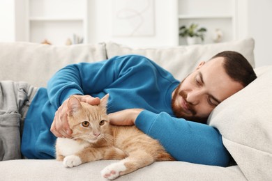 Man petting cute ginger cat on sofa at home