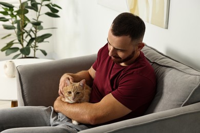 Photo of Man petting cute ginger cat on armchair at home