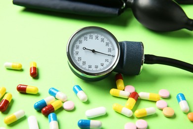 Photo of Blood pressure measuring device and pills on green background, closeup