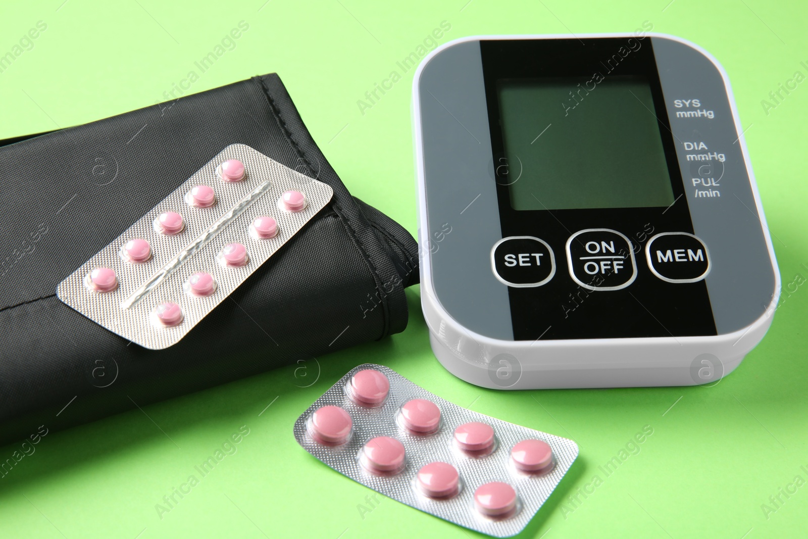 Photo of Blood pressure measuring device and pills on green background, closeup