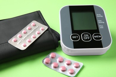 Photo of Blood pressure measuring device and pills on green background, closeup