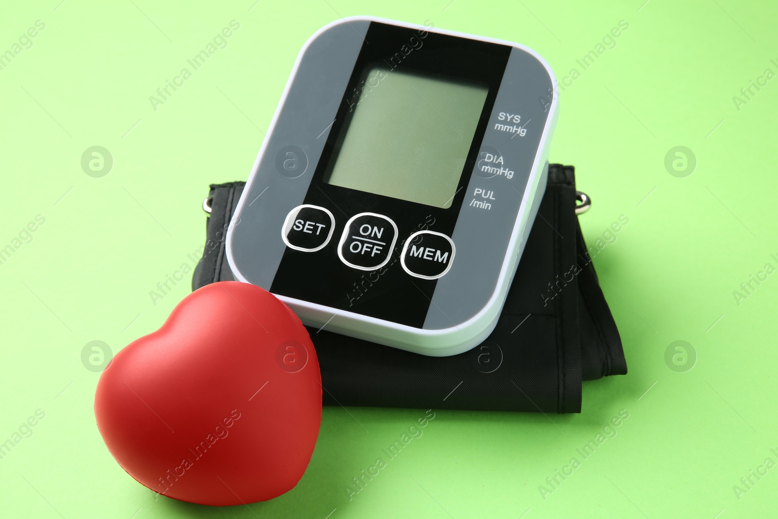 Photo of Blood pressure measuring device and squeeze heart on green background, closeup