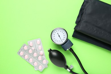 Photo of Blood pressure measuring device and pills on green background, top view. Space for text