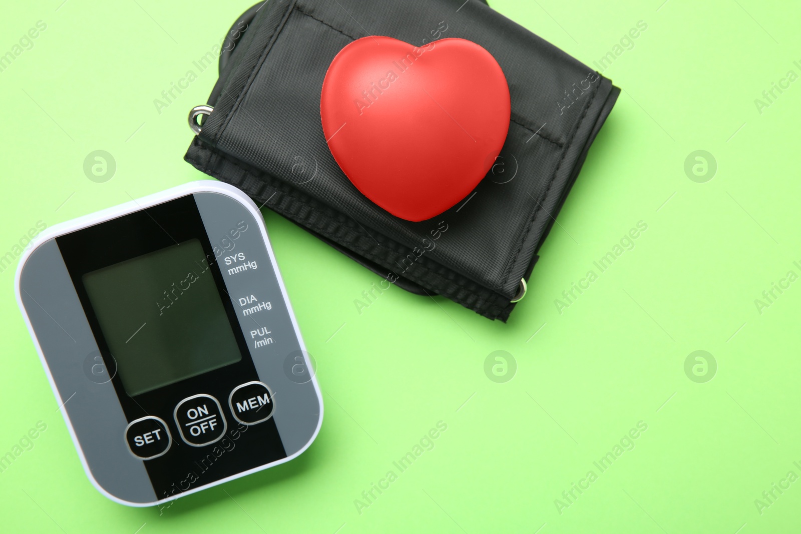 Photo of Blood pressure measuring device and squeeze heart on green background, top view