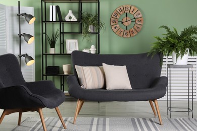 Photo of Comfortable sofa with pillows, armchair, shelving unit and houseplants in room