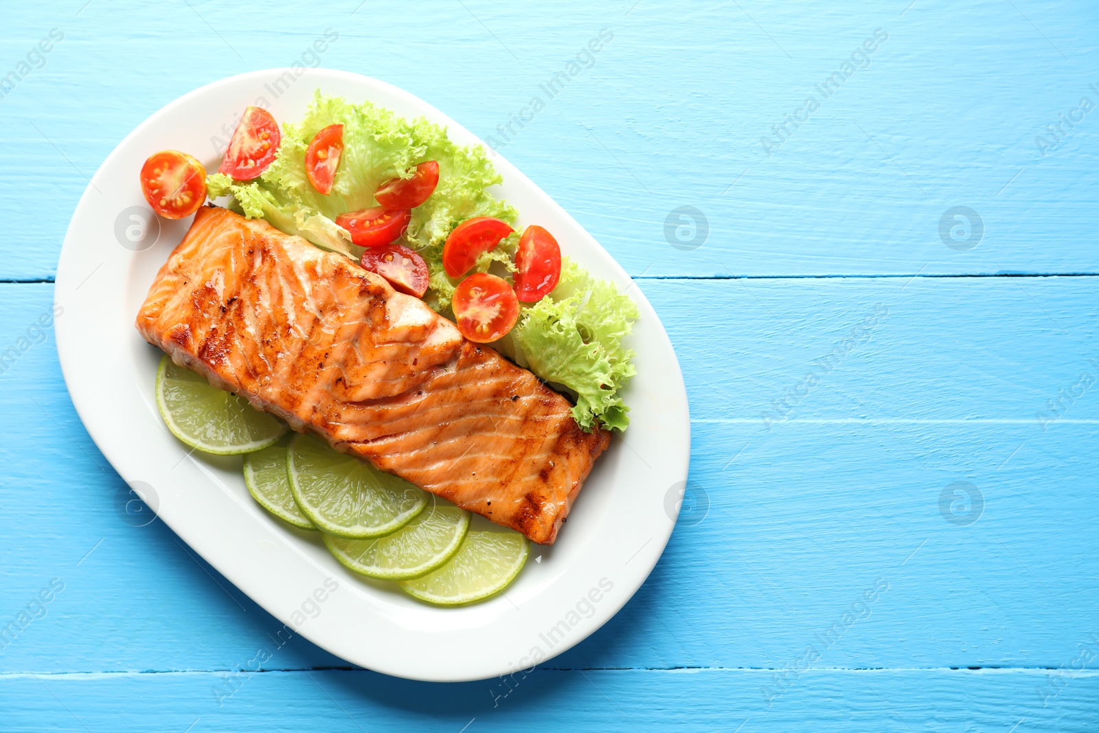 Photo of Delicious grilled salmon fillet with vegetable salad and lime on light blue wooden table, top view. Space for text