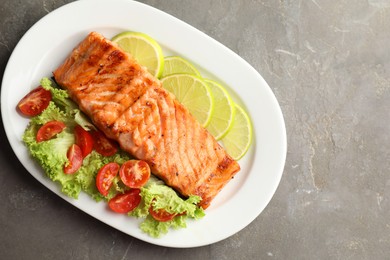 Photo of Delicious grilled salmon fillet with vegetable salad and lime on grey textured table, top view. Space for text