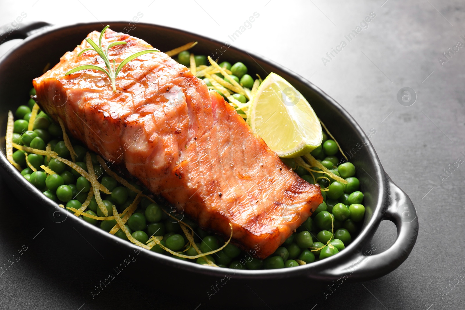 Photo of Delicious grilled salmon fillet with green peas and lime in baking dish on grey table, closeup