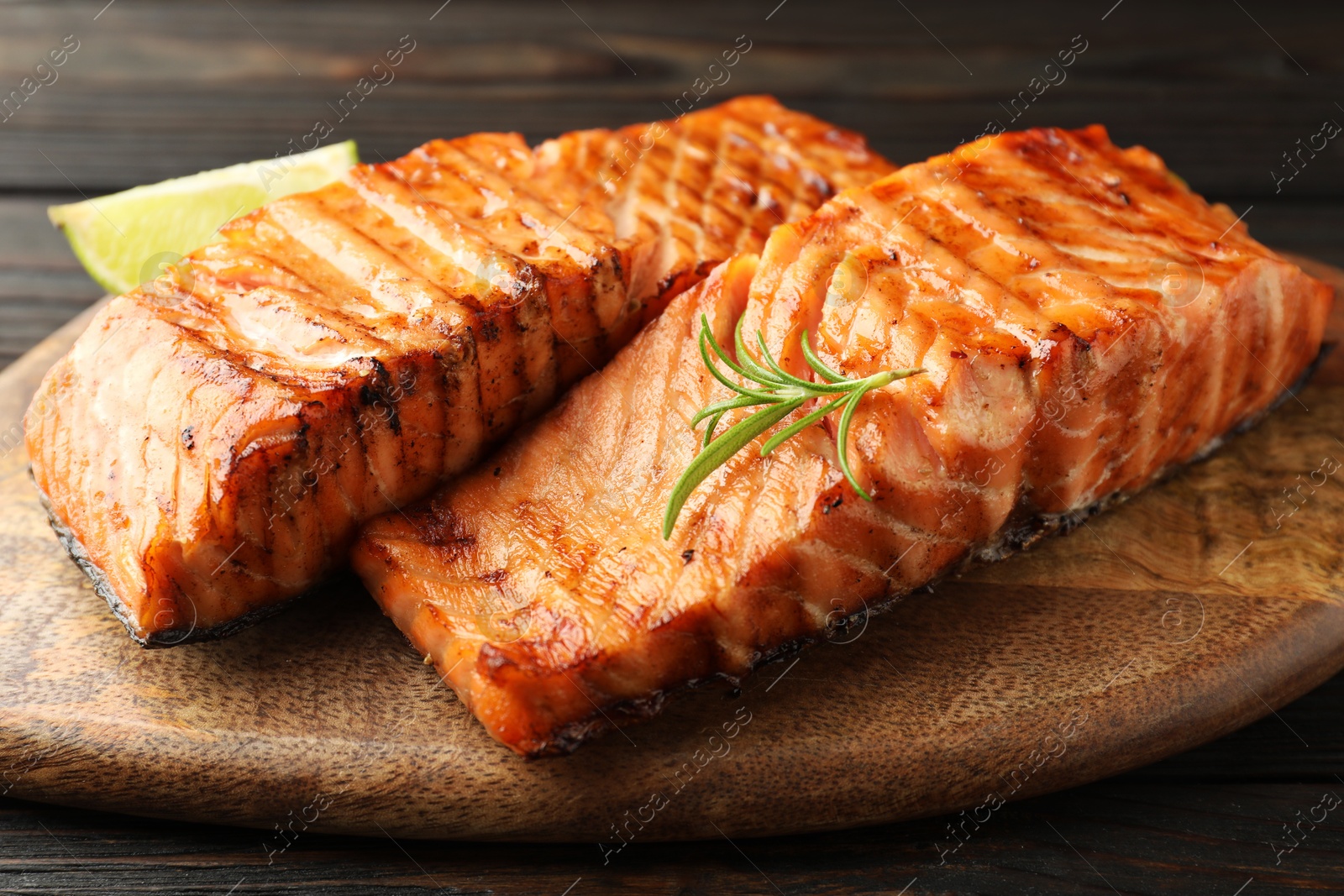 Photo of Delicious grilled salmon fillets with lime and rosemary on wooden table, closeup