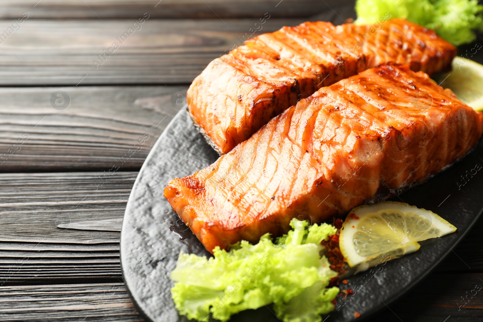 Photo of Delicious grilled salmon fillets with lettuce and lemon on wooden table, closeup