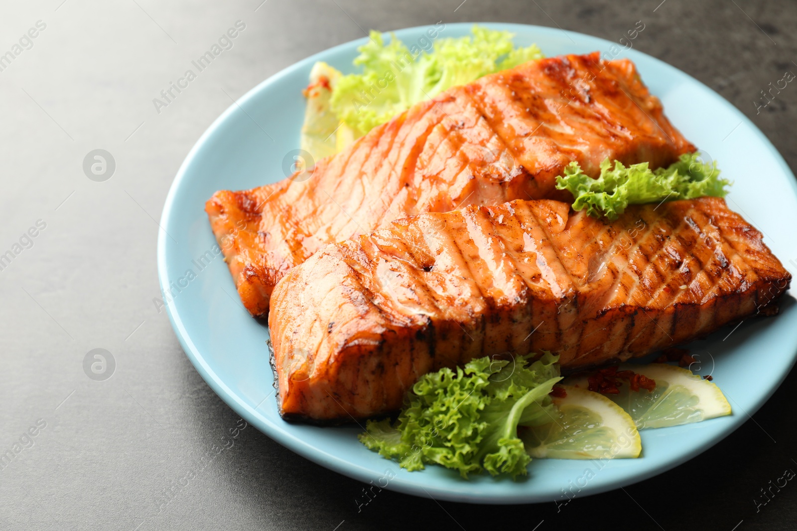 Photo of Delicious grilled salmon fillets with lettuce and lemon on grey table, closeup