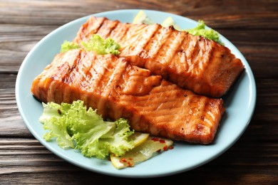 Photo of Delicious grilled salmon fillets with lettuce and lemon on wooden table, closeup