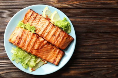 Photo of Delicious grilled salmon fillets with lettuce and lemon on wooden table, top view. Space for text