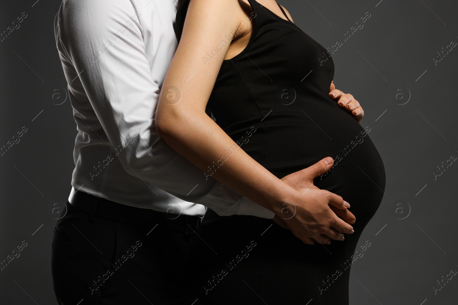 Photo of Pregnant woman with her husband touching belly on grey background, closeup