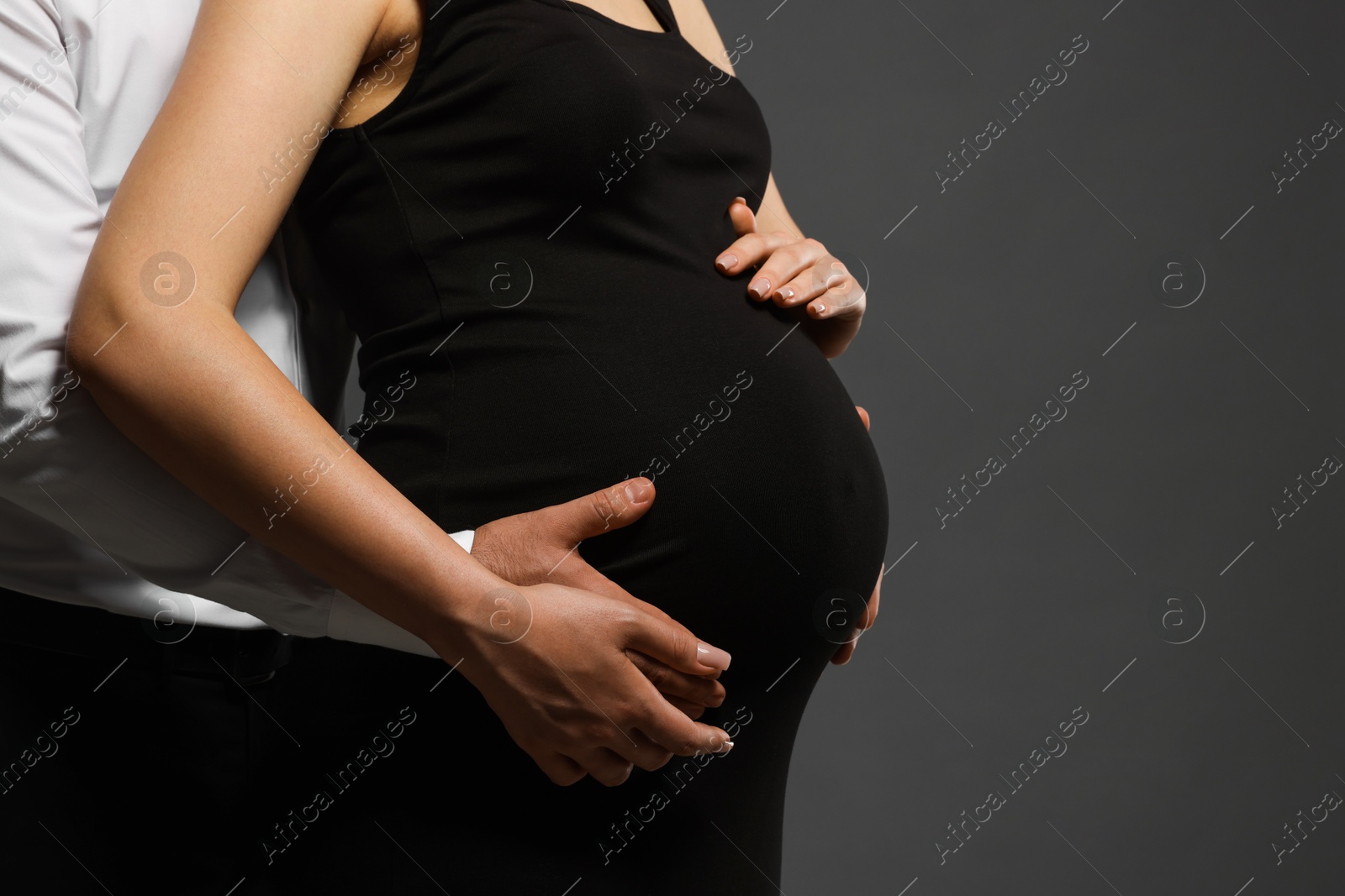 Photo of Pregnant woman with her husband touching belly on grey background, closeup. Space for text