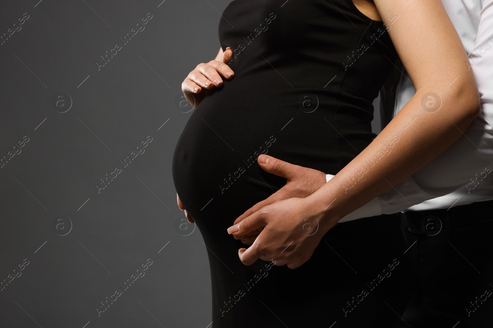 Photo of Pregnant woman with her husband touching belly on grey background, closeup. Space for text