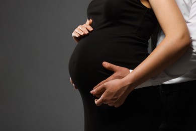 Photo of Pregnant woman with her husband touching belly on grey background, closeup. Space for text