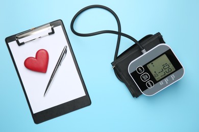 Photo of Blood pressure measuring device, clipboard with pen and heart figure on light blue background, flat lay