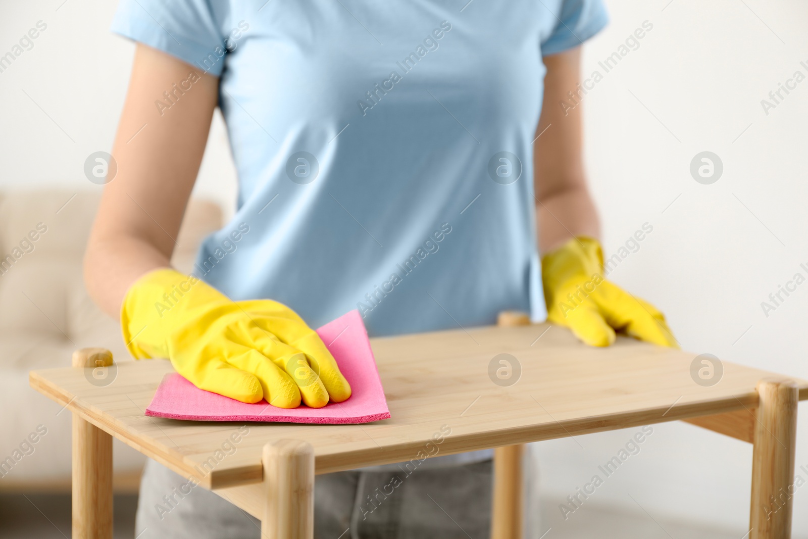 Photo of Young woman cleaning wooden shelf with rag at home, closeup