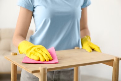 Young woman cleaning wooden shelf with rag at home, closeup