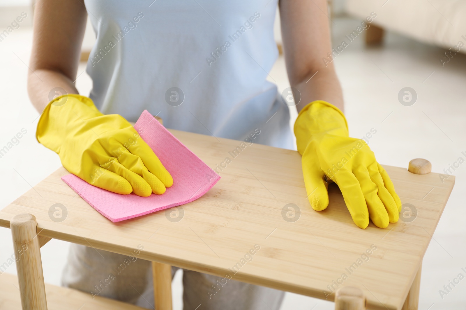 Photo of Young woman cleaning wooden shelf with rag at home, closeup