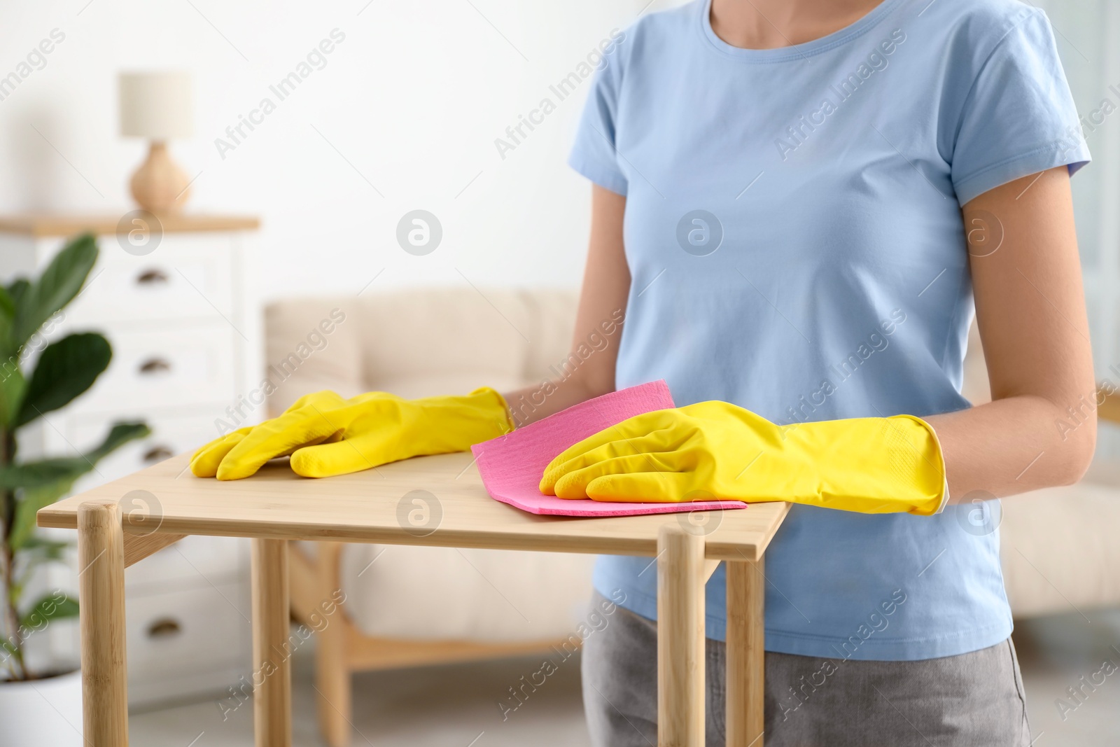 Photo of Young woman cleaning wooden shelf with rag at home, closeup