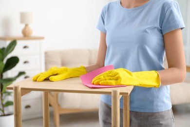 Photo of Young woman cleaning wooden shelf with rag at home, closeup