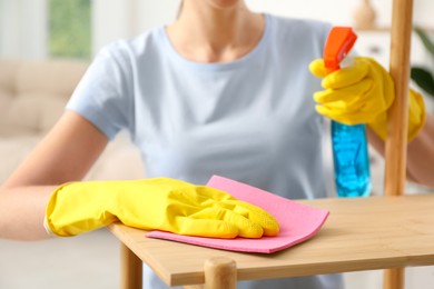 Young woman cleaning wooden shelf with rag and spray at home, closeup