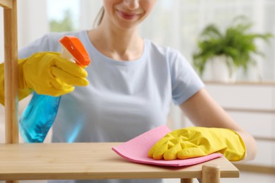 Young woman cleaning wooden shelf with rag and spray at home, closeup