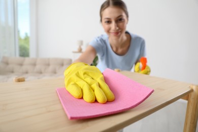 Young woman cleaning wooden shelf with rag and spray at home, selective focus