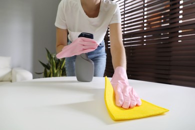 Young woman cleaning table with rag and spray in office, closeup