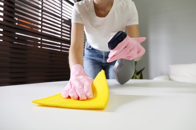 Young woman cleaning table with rag and spray in office, closeup