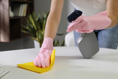 Young woman cleaning table with rag and spray in office, closeup