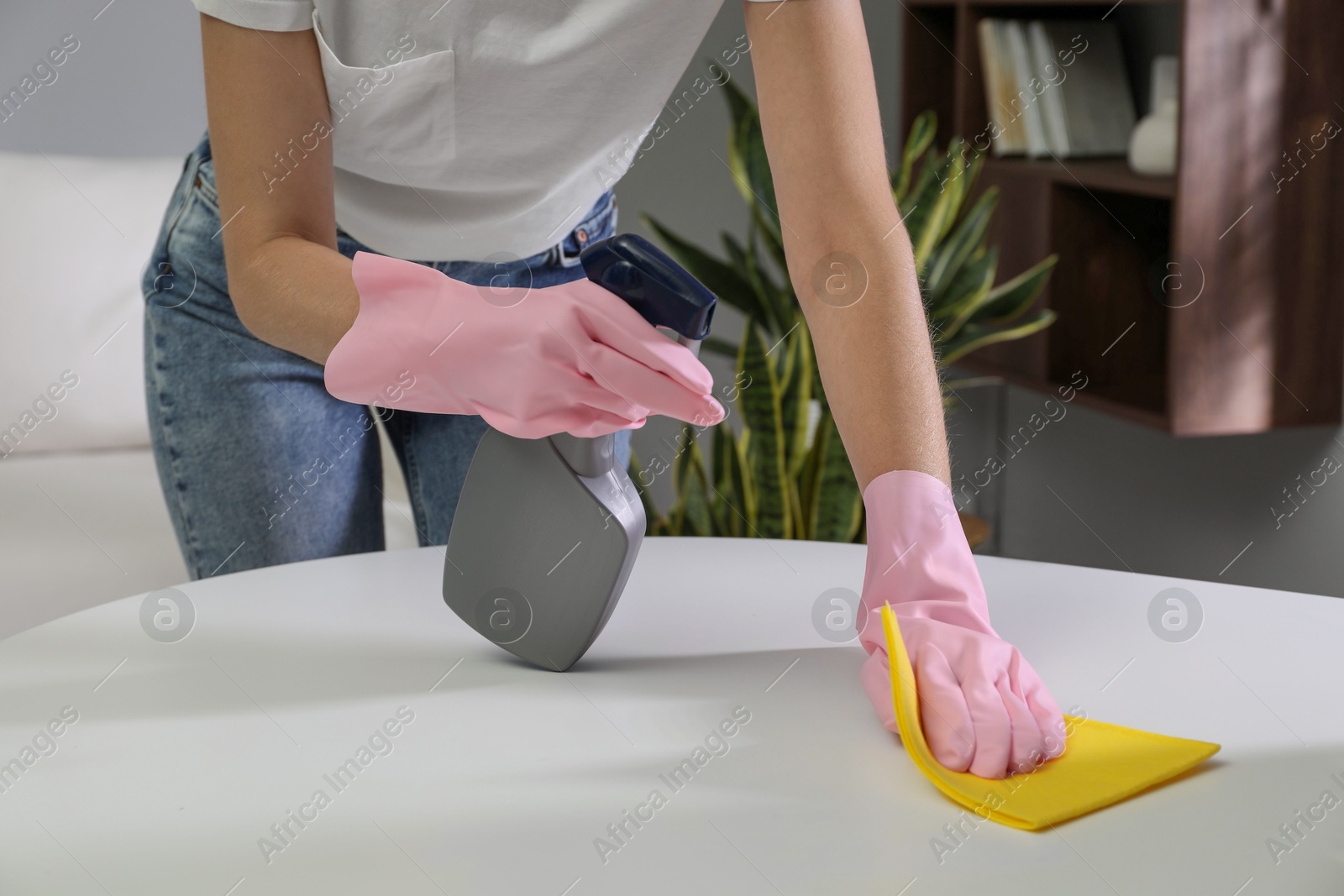 Photo of Young woman cleaning table with rag and spray in office, closeup