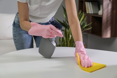 Photo of Young woman cleaning table with rag and spray in office, closeup