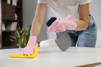 Young woman cleaning table with rag and spray in office, closeup