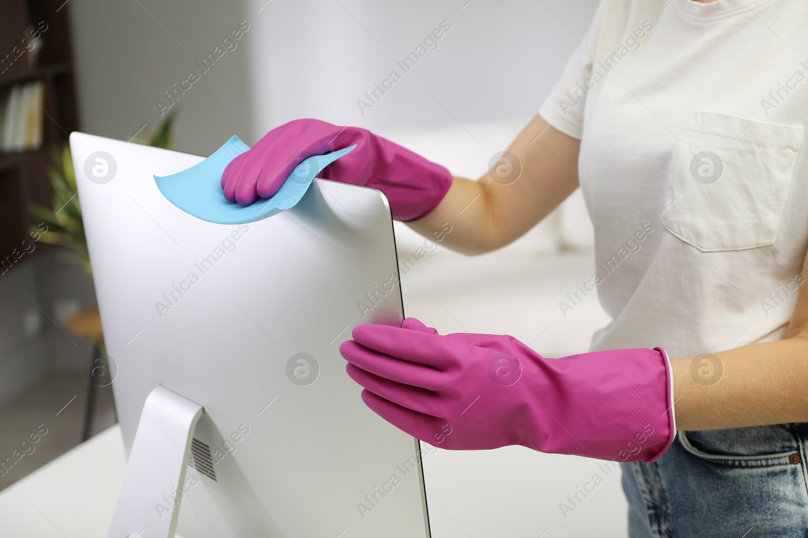 Photo of Young woman cleaning computer with rag and spray in office, closeup