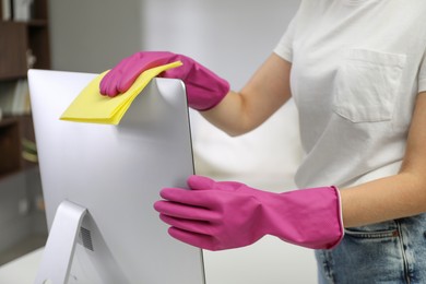 Photo of Young woman cleaning computer with rag and spray in office, closeup