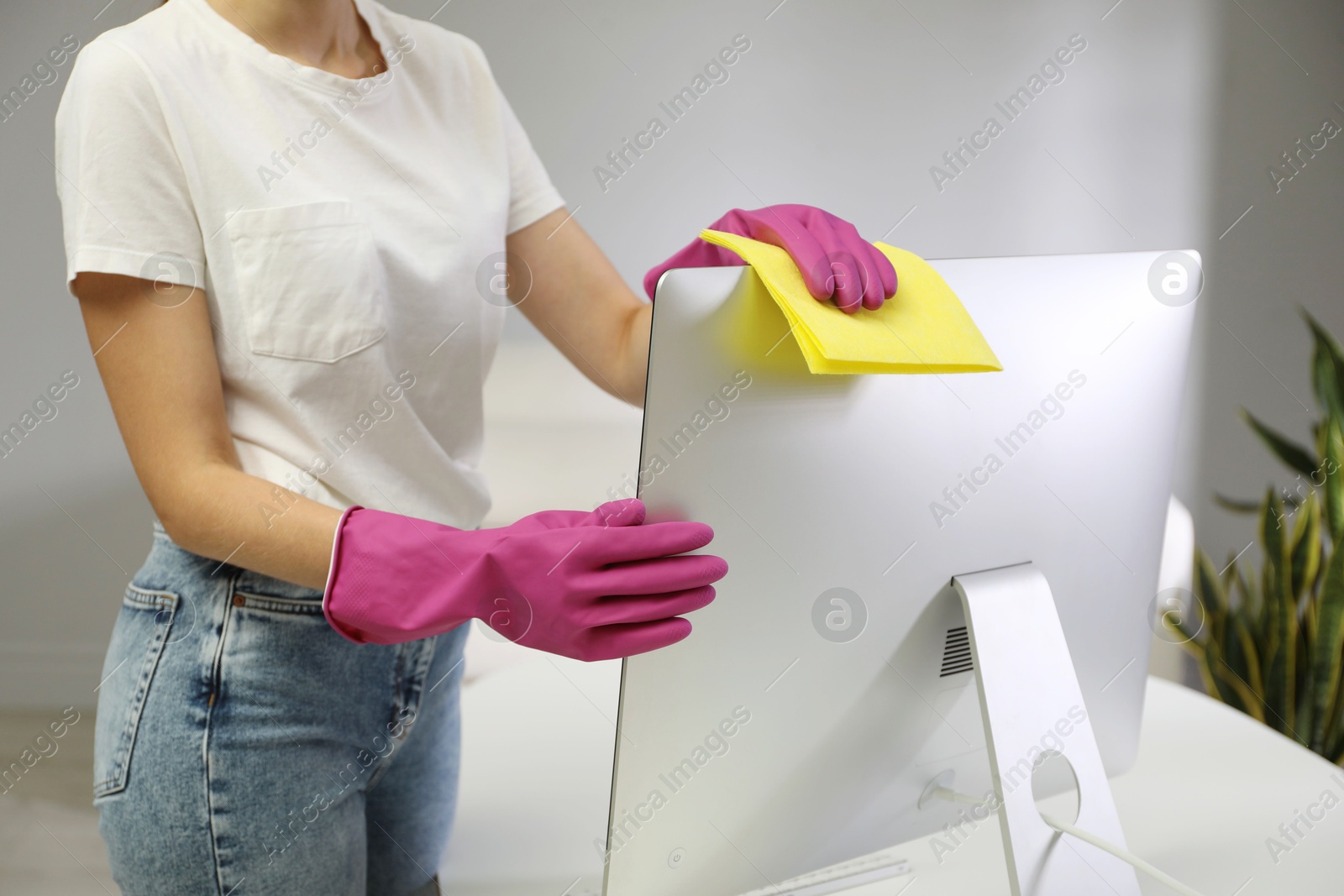 Photo of Young woman cleaning computer with rag and spray in office, closeup