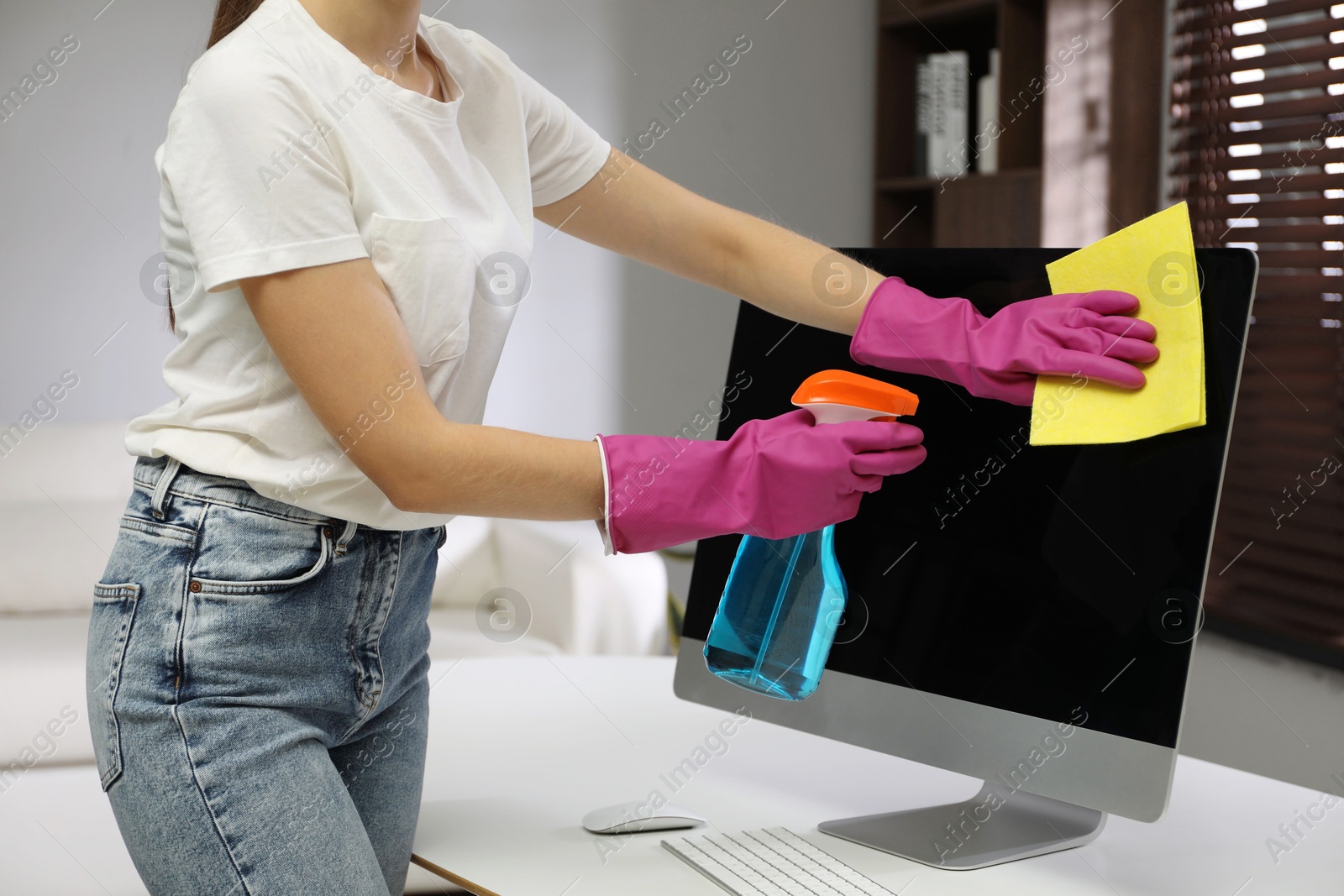 Photo of Young woman cleaning computer with rag and spray in office, closeup