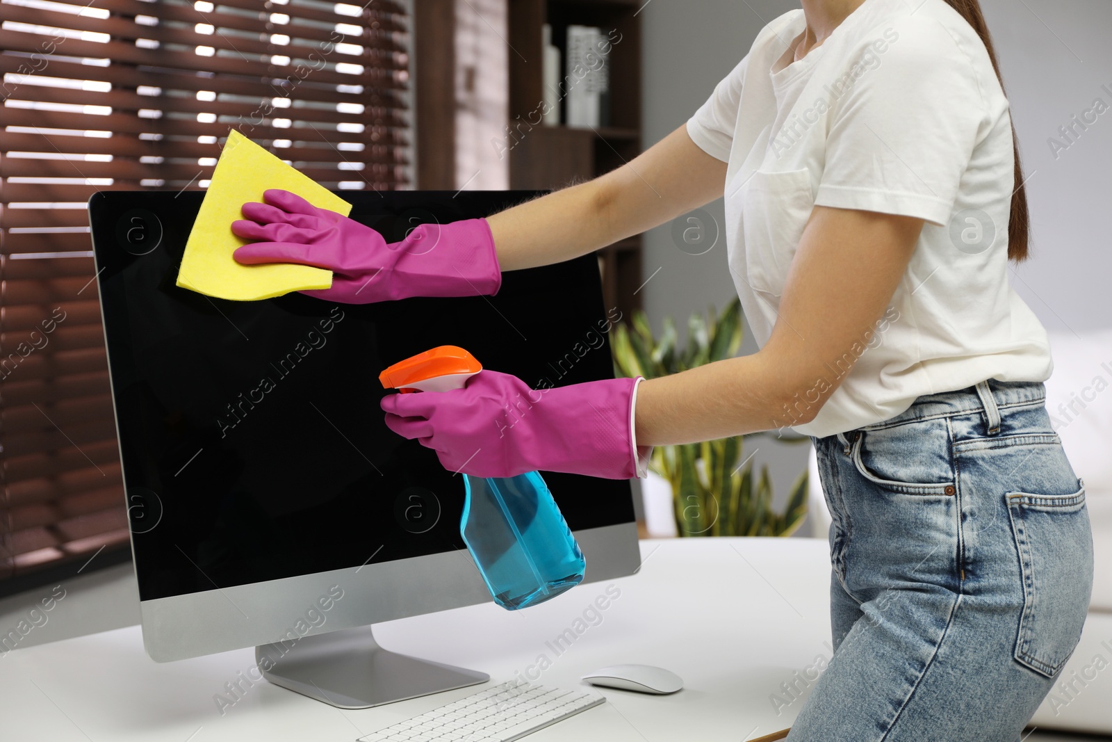 Photo of Young woman cleaning computer with rag and spray in office, closeup