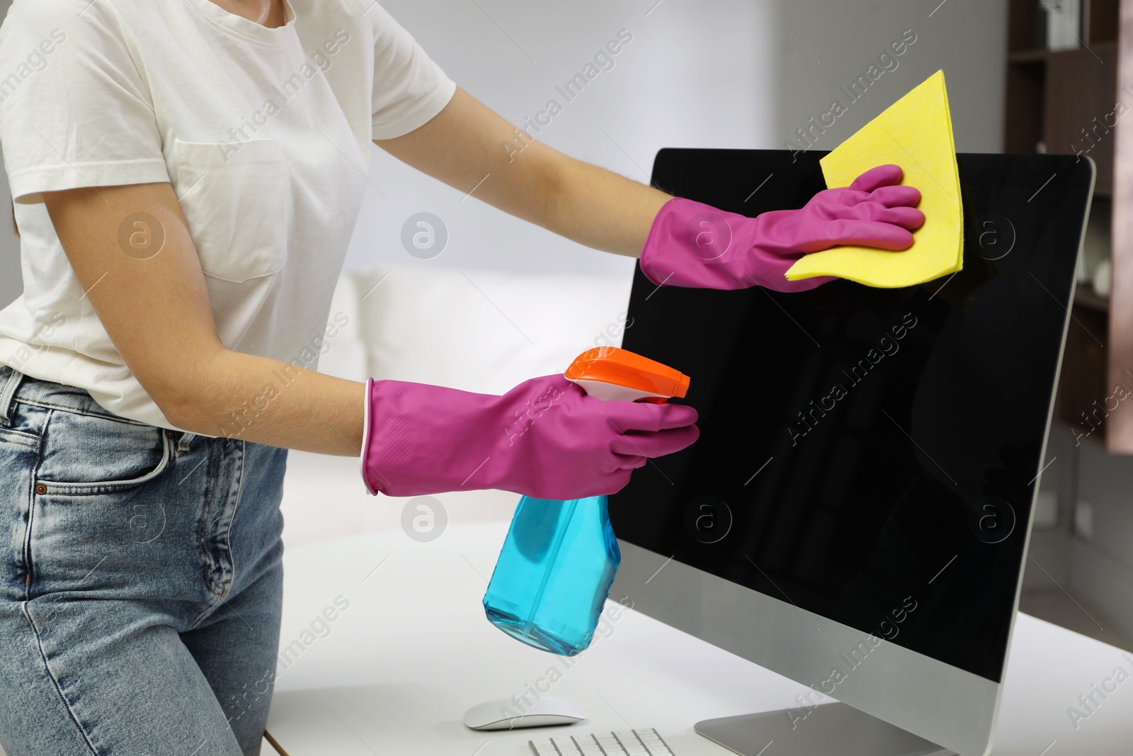 Photo of Young woman cleaning computer with rag and spray in office, closeup