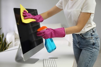 Photo of Young woman cleaning computer with rag and spray in office, closeup