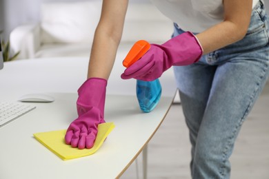 Photo of Young woman cleaning table with rag and spray in office, closeup