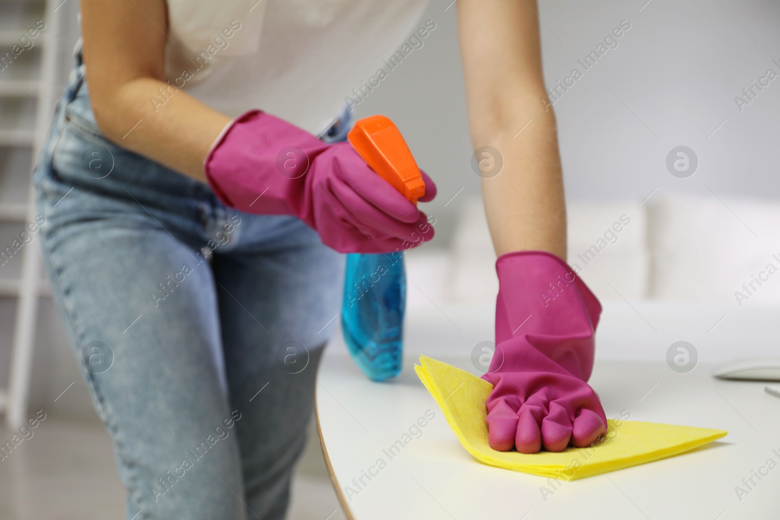 Photo of Young woman cleaning table with rag and spray in office, closeup