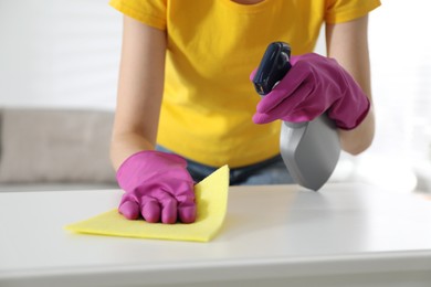 Young woman cleaning table with rag and spray in office, closeup