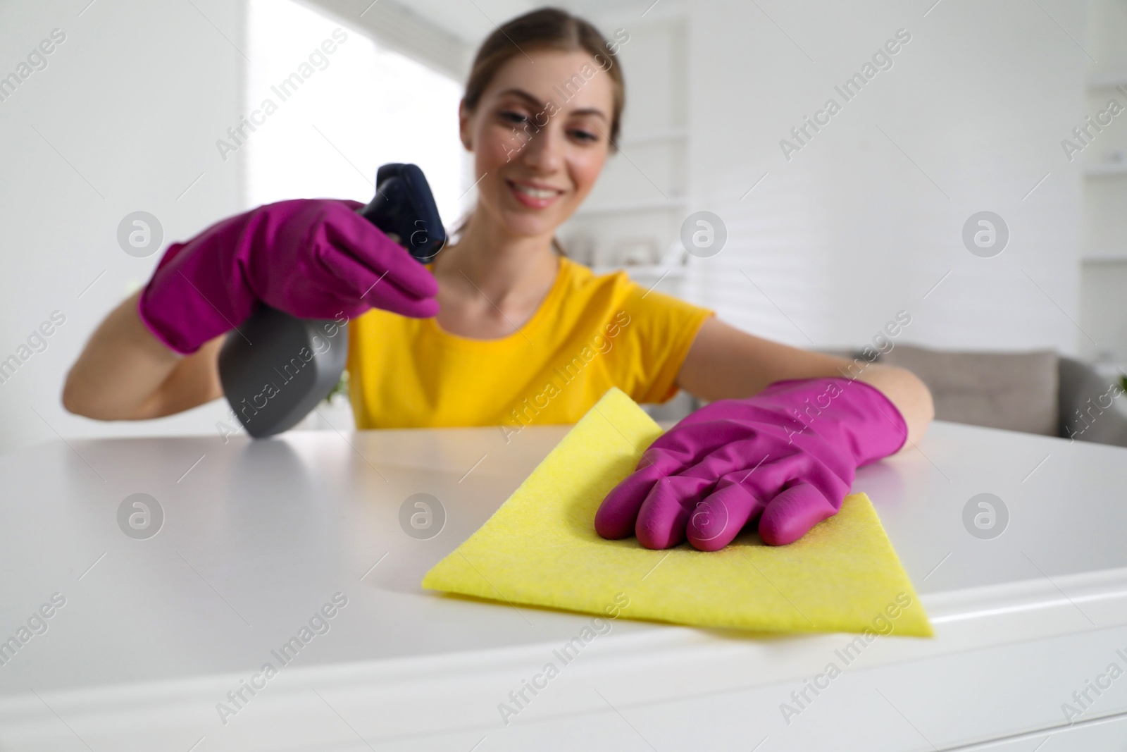 Photo of Young woman cleaning table with rag and spray in office, selective focus