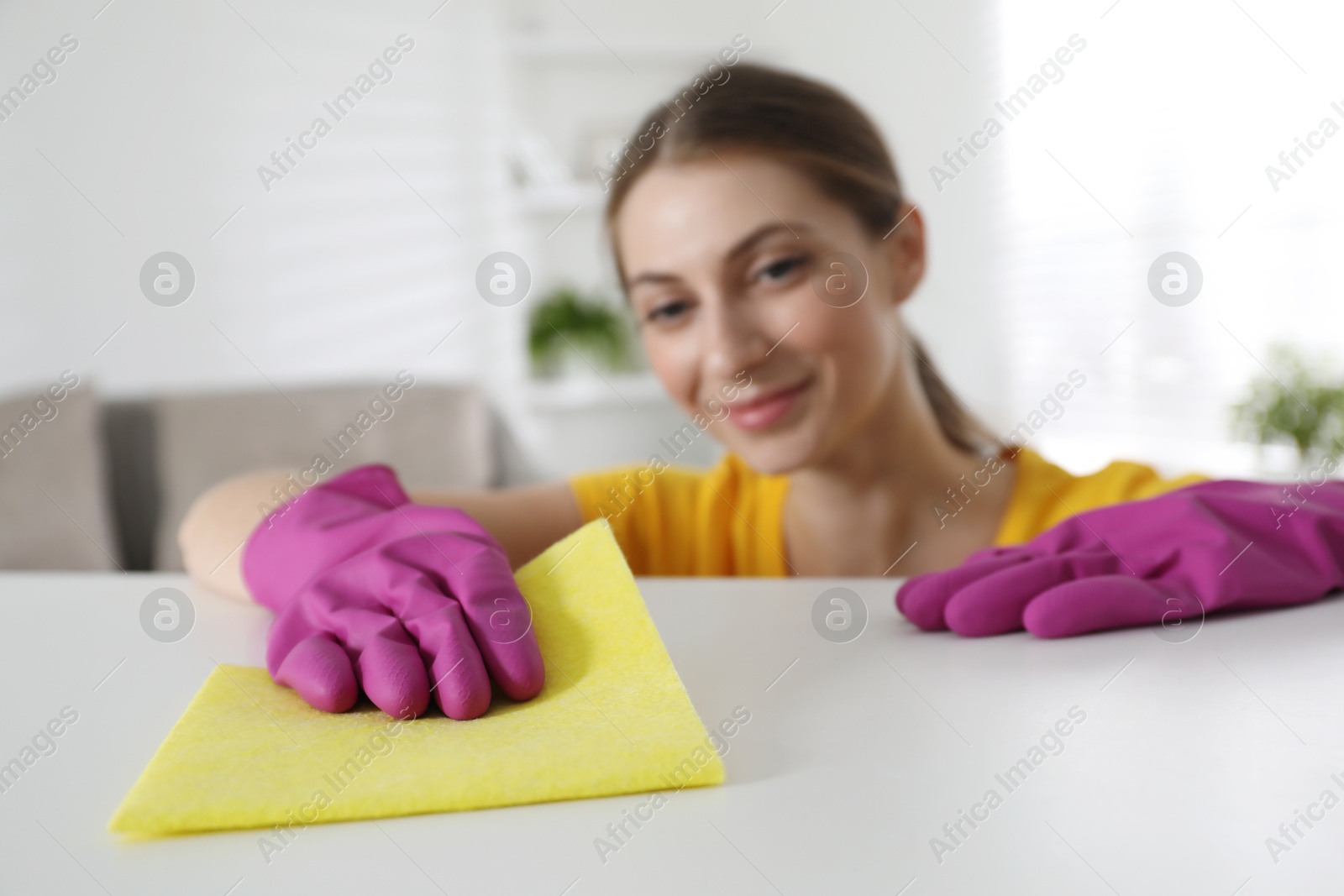 Photo of Young woman cleaning table with rag in office, selective focus